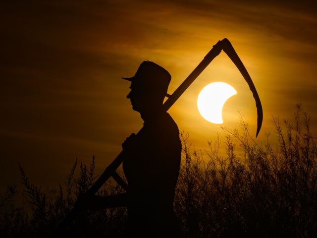 Bauer mit Sense auf dem Feld während der partiellen Sonnenfinsternis