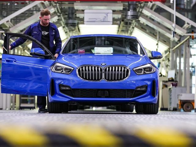 Ein Firmenmitarbeiter stehet neben einem blauen BMW 1er, der im BMW Group Werk Leipzig vom Band läuft.