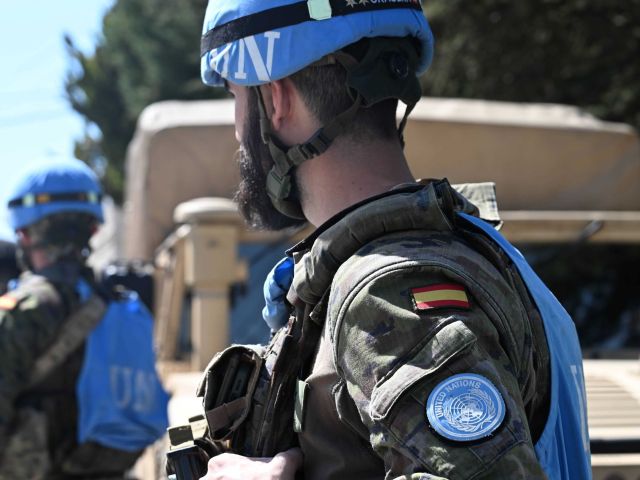 Ein Soldat ist von hinten zu sehen. Er trägt eine blaue Weste mit der Aufschrift UN und hat einen blauen Überzug über seinem Helm.