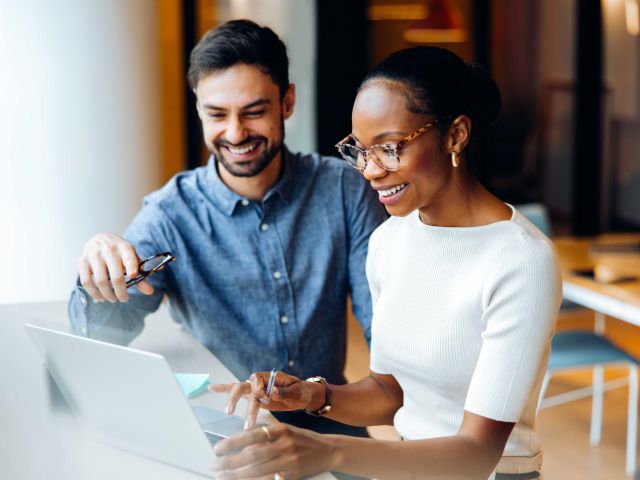 Two professionals at a desk using a laptop in a bright office setting