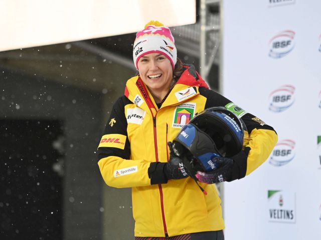 Portrait der deutschen Bobfahrerin Laura Nolte. Sie trägt die offizielle Kleidung des deutschen Wintersportteams und hält ihren Bob-Helm unter dem Arm.