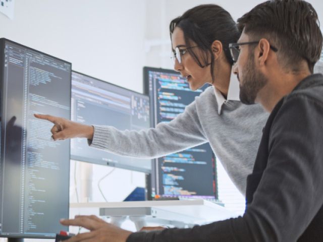 Frau und Mann in Büro vor mehreren Computerbildschirmen 