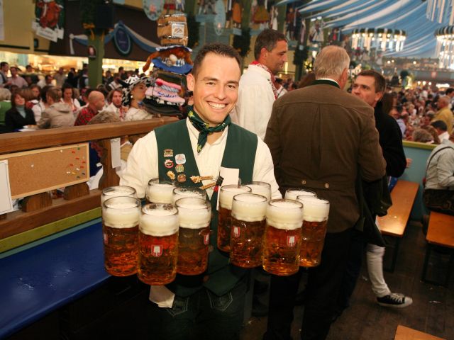 Ein Mann hält 12 Maß Bier in der Hand und lächelt
