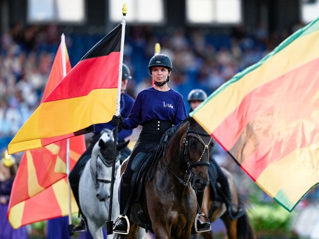 Eine Reiterin sitzt auf einem Pferd und hält Flaggen in der Hand.