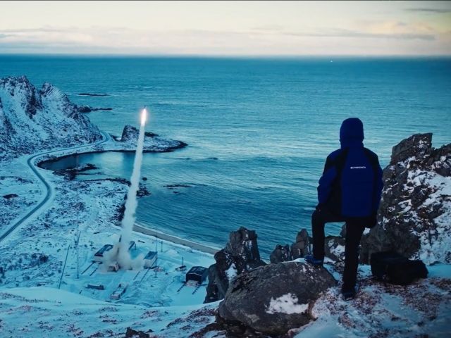 Eine Person steht auf einem Hügel einer Schneelandschaft und blickt auf einen Raketenstart.