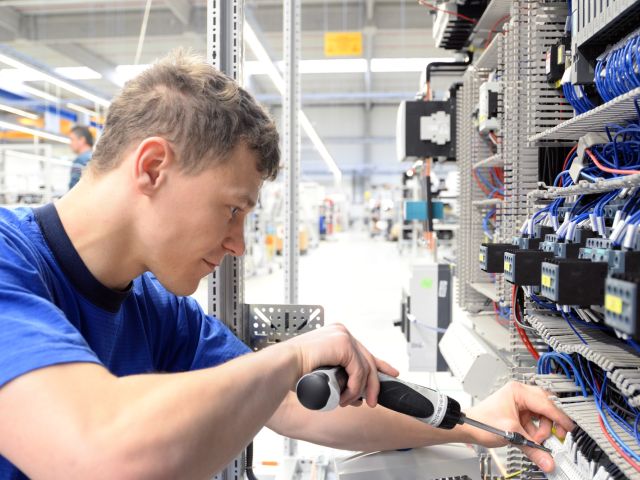 junger Lehrling montiert Komponenten und Kabel in einer Fabrik in einem Schaltschrank - Arbeitsplatzindustrie mit Zukunft 