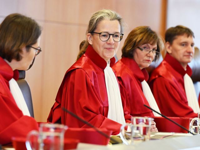 Drei Frauen und ein Mann in roten Roben sitzen an einem Tisch.