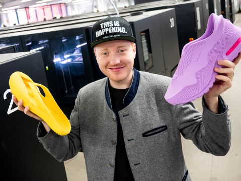 Ein junger Mann hält zwei Schuhe aus dem 3D-Drucker 