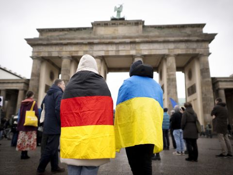 Eine Person mit einer Deutschland- und eine Person mit einer Ukraine-Flagge um die Schulter stehen vor dem Brandenburger Tor in Berlin