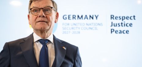 Un hombre se encuentra ante una pantalla en la que se lee “Germany for UN Security Council 2027/2028”.