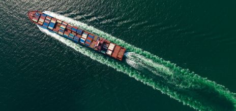 Aerial photograph of a container ship travelling across the sea, creating a wide wake.