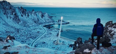 A person stands on a hill in a snowy landscape and watches a rocket launch.