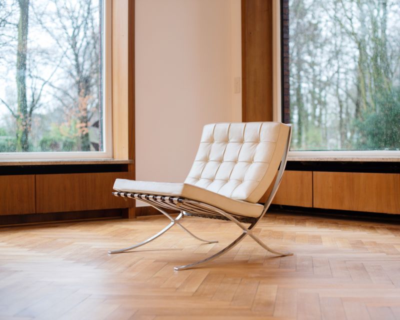 Barcelona-Sessel von Ludwig Mies van der Rohe und Lilly Reich aus dem Jahr 1929 steht in einem Raum mit Parkett und großen Fenstern.