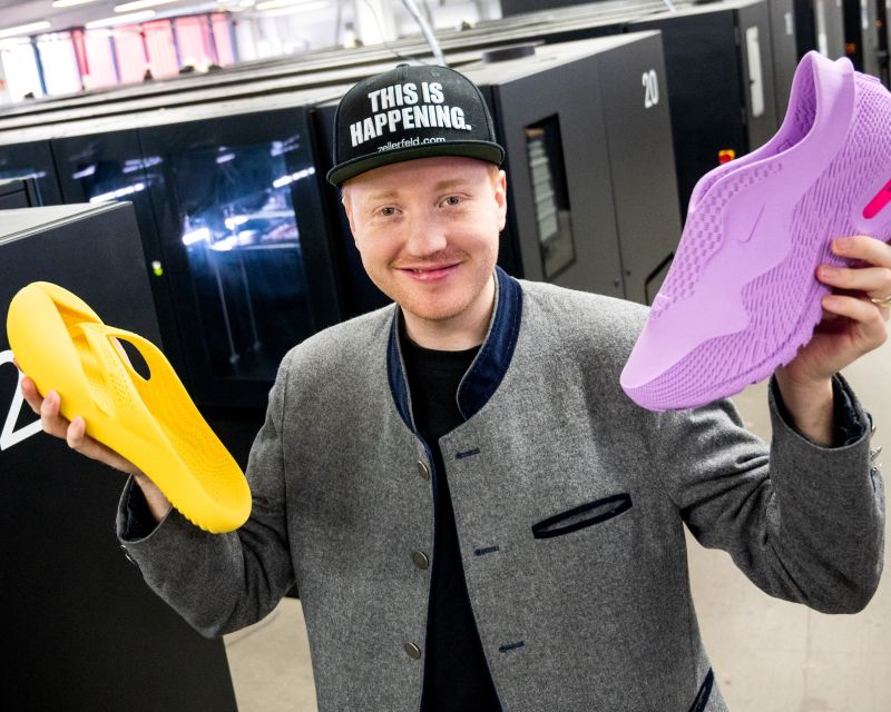 Ein junger Mann hält zwei Schuhe aus dem 3D-Drucker 