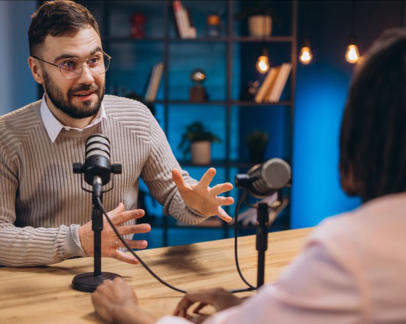 Ein Mann und eine Frau diskutieren an einem Tisch mit Mikrofonen.