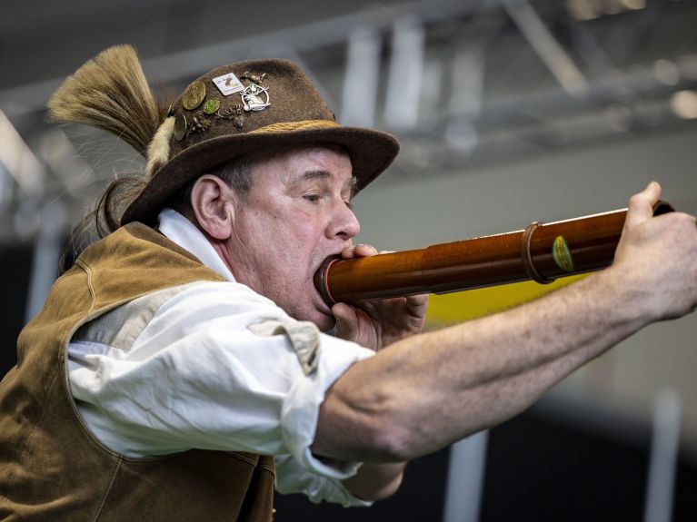 A man in traditional dress holds a tube to his mouth.