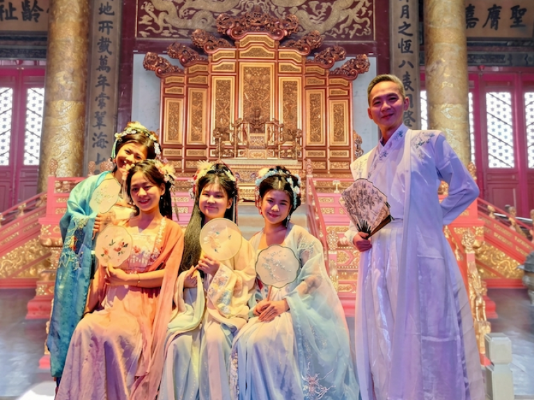 Familie Lam in traditioneller chinesischer Kleidung posieren mit Fächern in einer chinesischen Palasthalle. 