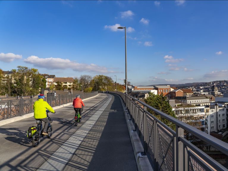 Two cyclists on the Nordbahntrasse in Wuppertal, a wide cycling and walking path built on a former railway line, overlooking the city. 