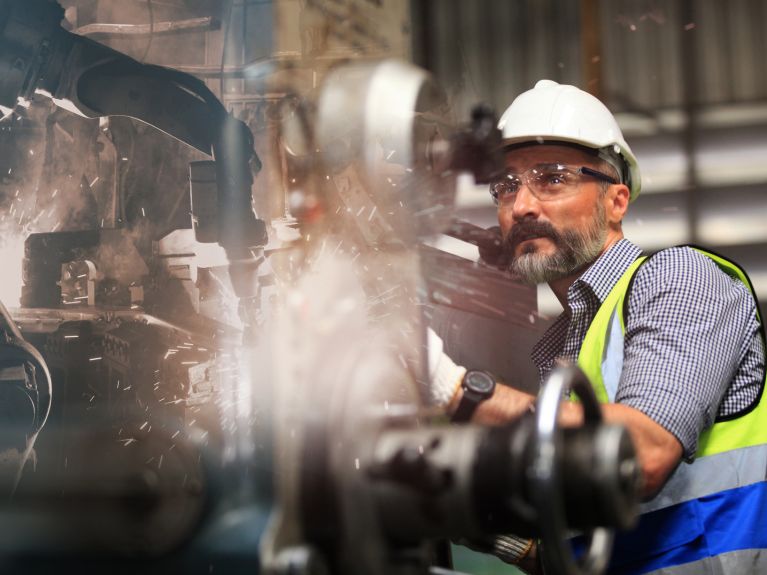 Mann mit Helm und Schutzbrille an einer Produktionsmaschine