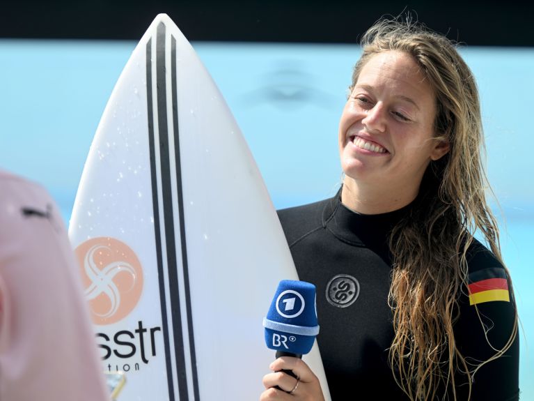 Eine Frau hält Surfbrett und ein Mikrofon
