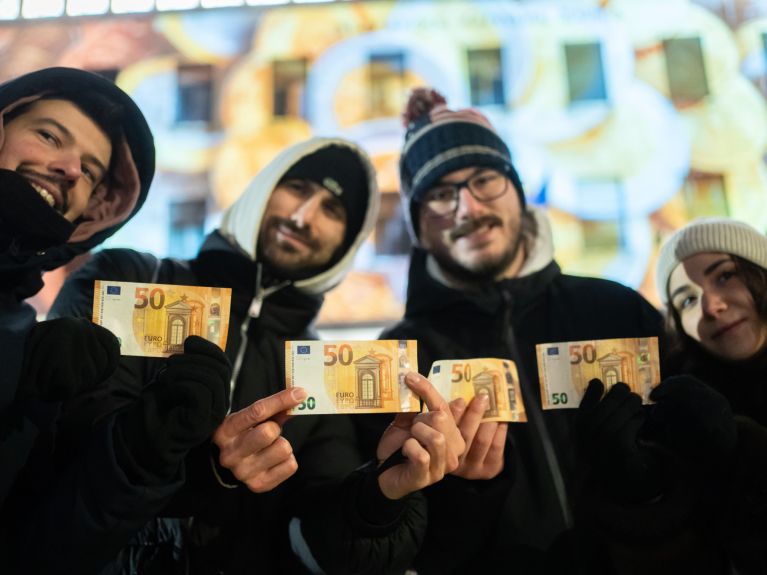 Vier junge Menschen in Winterkleidung halten jeweils einen 50 Euro Schein in die Kamera.