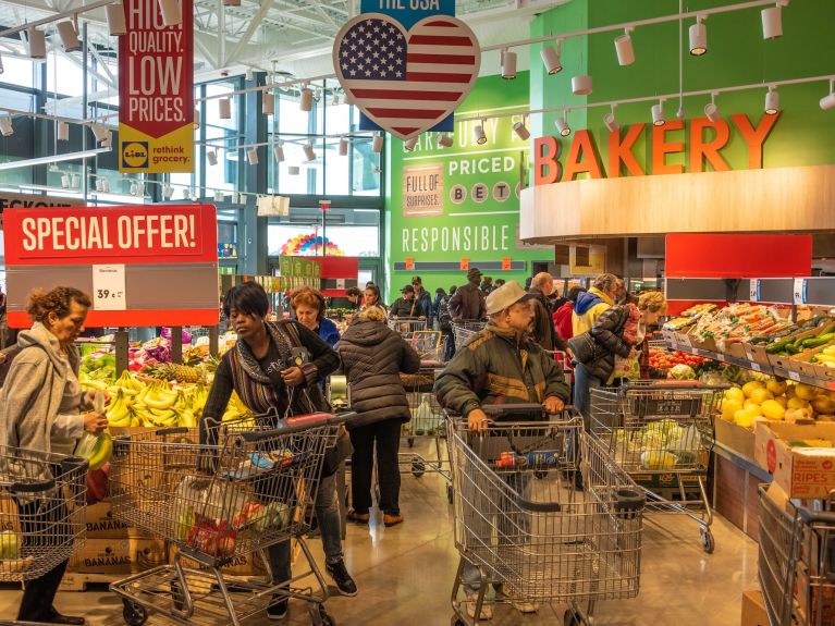 Menschen mit Einkaufswagen laufen durch einen Supermarkt. 