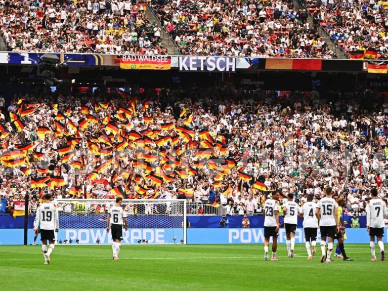 Deutsche Fußballspieler laufen nach dem Spiel über den Rasen in Richtung Fanblock, in dem zahlreiche Fans mit schwarz-rot-goldenen Fahnen jubeln. 