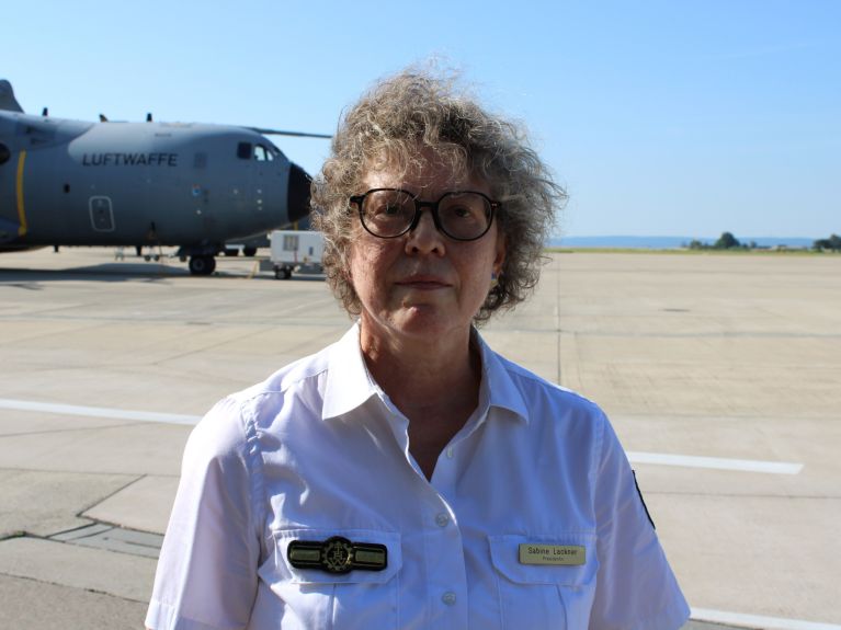 Una mujer está en un aeródromo; detrás de ella, un avión de las Fuerzas Aéreas alemanas