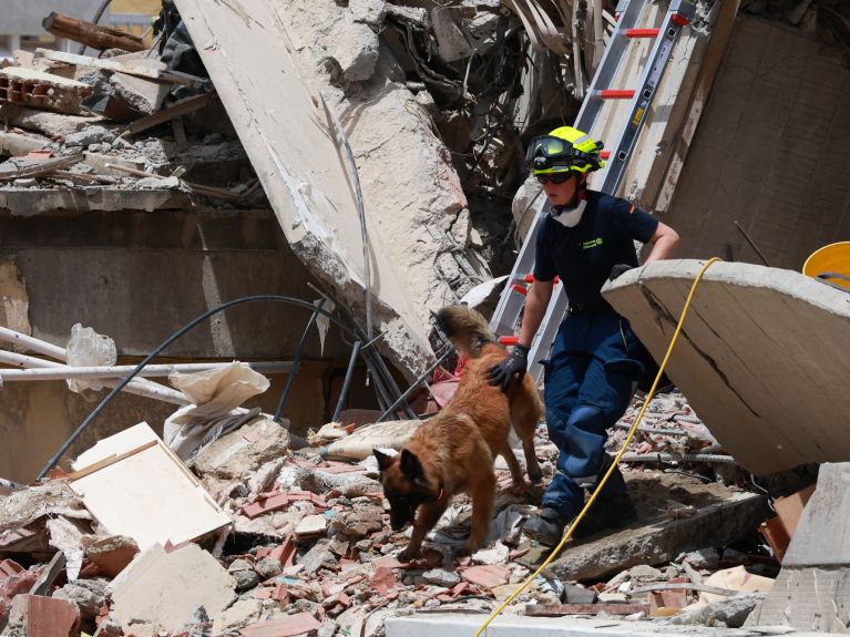 Una mujer y un perro de búsqueda recorren los escombros de un edificio.