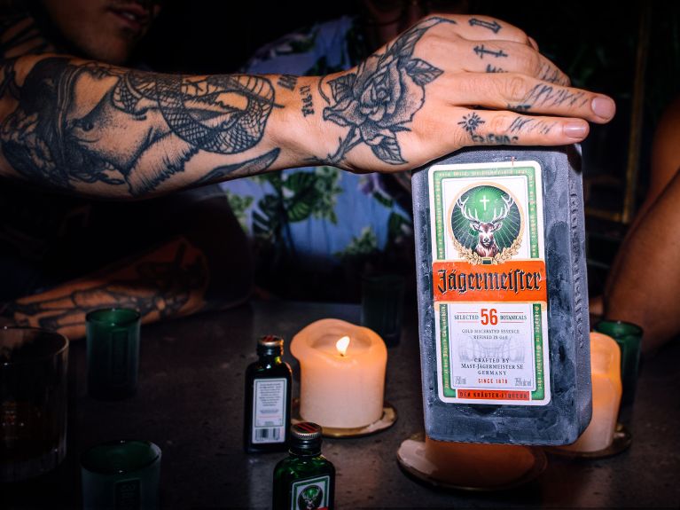Tätowierter Arm und Hand mit gefrohrener Jägermeisterflasche 