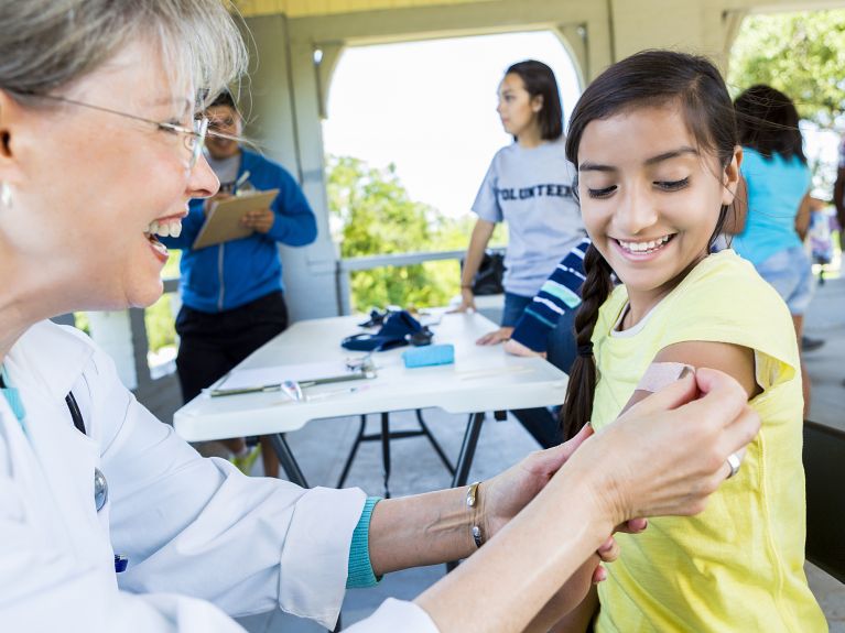 Smiling doctor, senior woman, and little girl, hispanic. They are both smiling as she gets her bandaid placed on. 