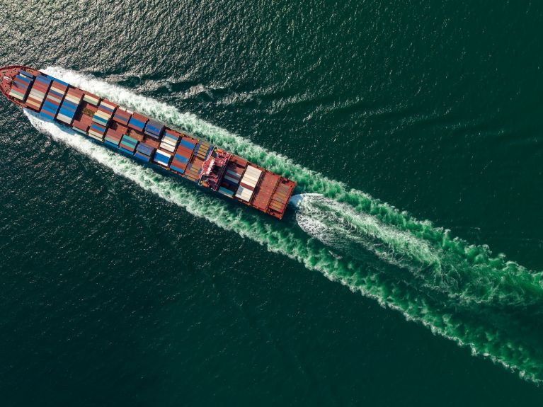 Aerial photograph of a container ship travelling across the sea, creating a wide wake.