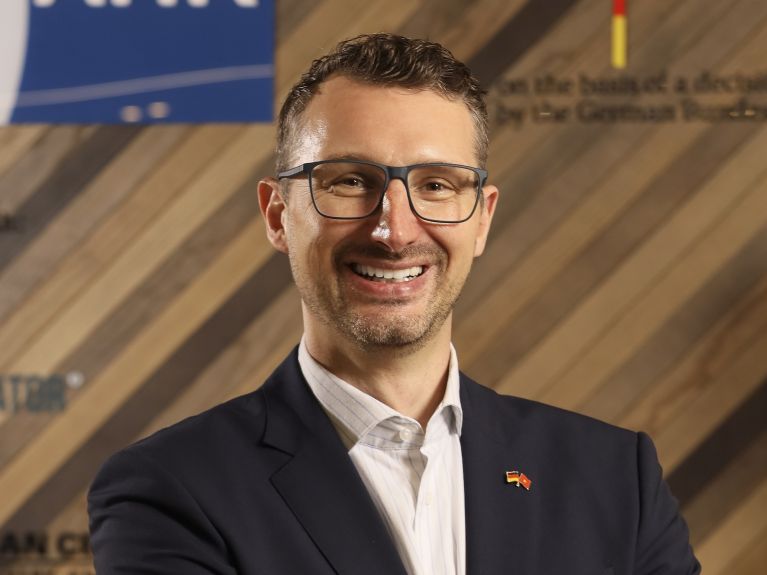 A man in a suit looks into the camera. “AHK Vietnam” can be read on the picture.