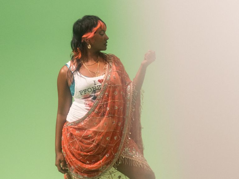 A young woman with red streaks in her black hair wears a vest top with the slogan “I love Pforzheim” and over it a garment with a Tamil-inspired look.