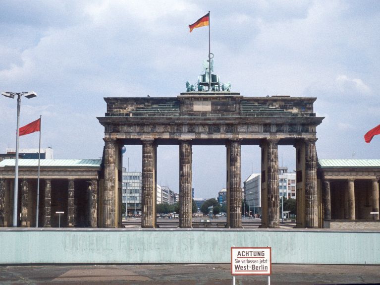 1980: Ein Blick von West-Berlin über die Mauer zum Brandenburger Tor in Ost-Berlin. Schild im Vordergrund: „Achtung, Sie verlassen jetzt West-Berlin.“ 1980: Ein Blick von West-Berlin über die Mauer zum Brandenburger Tor in Ost-Berlin. Schild im Vordergrund: „Achtung, Sie verlassen jetzt West-Berlin.“