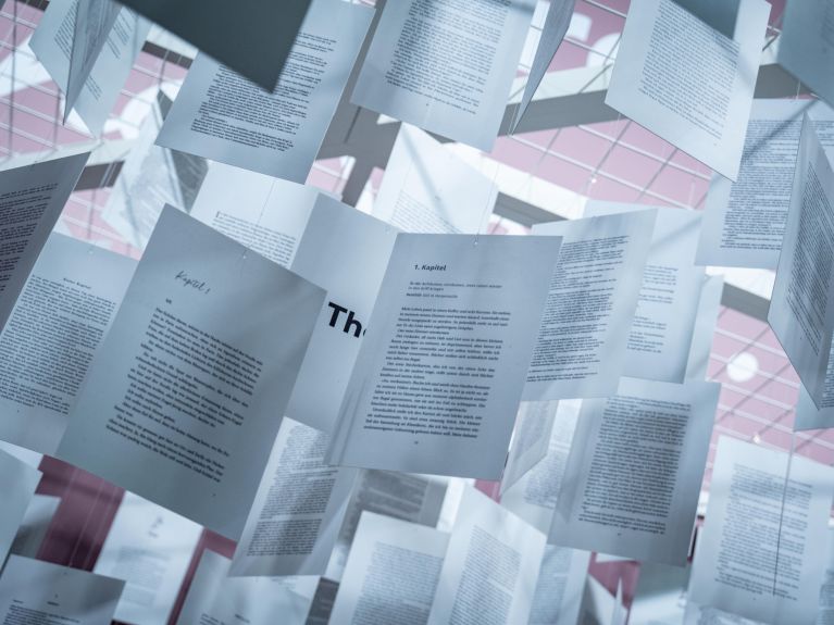 Buchseiten hängen an Fäden von der Decke. 