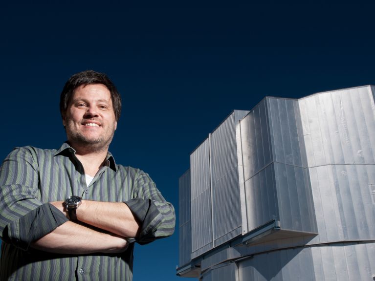 Ein Mann steht neben einem Gebäude und lächelt in die Kamera.