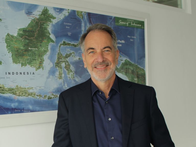A man stands in front of a map of Indonesia.