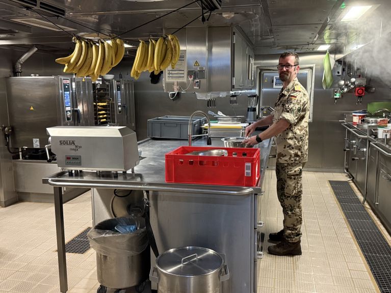 A man in uniform is standing at the hob in a kitchen. 