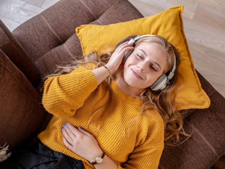 Una mujer joven con los ojos cerrados y auriculares acostada en un sofá