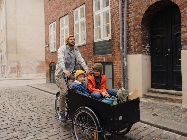 A man on a cargo bike transporting two children through the city.