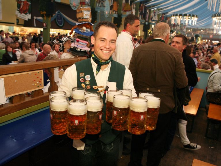A man holds 12 beer mugs in his hand and smiles