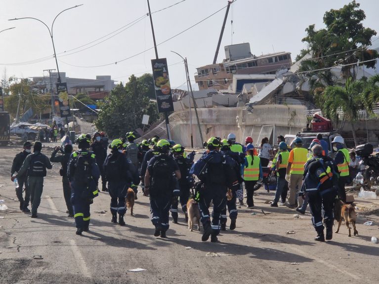 Se ve a varias personas de espaldas mientras caminan entre los escombros. 