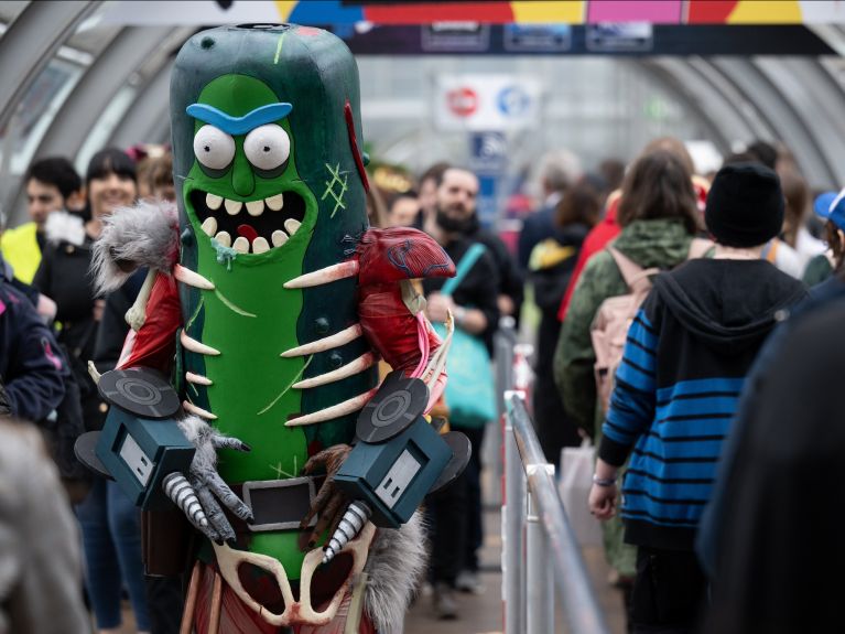 A cosplayer is dressed as “Pickle Rick”, and visitors to the fair can be seen alongside him.