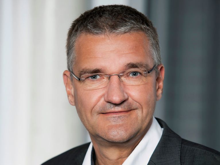 Mann mit kurzen grauen Haaren und Brille. 