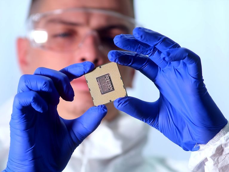 Ein Mann in Schutzanzug und mit Handschuhen hält einen Chip in der Hand.