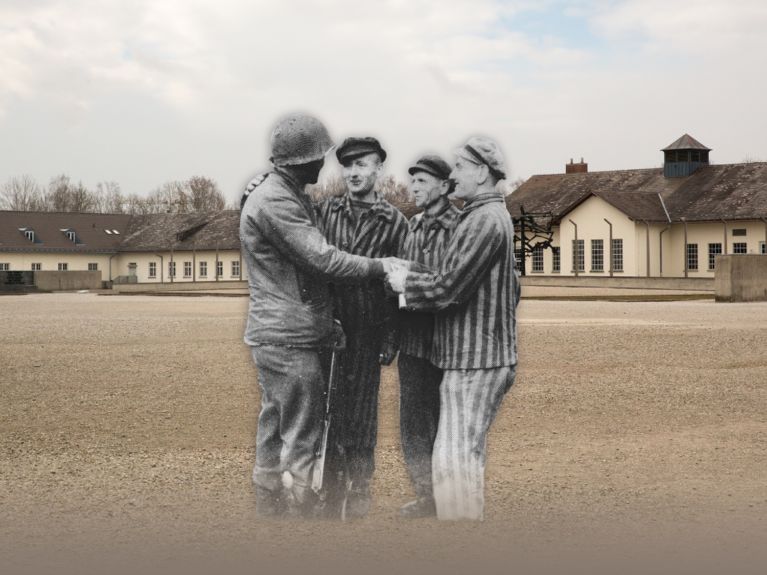 Więźniowie podpierają się o siebie nawzajem przed barakami KL Dachau.