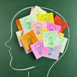 Hay una cabeza pintada en una pizarra, sobre la que hay notas adhesivas con bombillas.