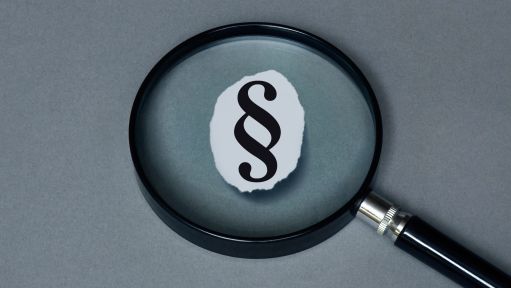 Fotompontage: Unter einer Lupe befindet sich das Symbol eines Paragrafenzeichen