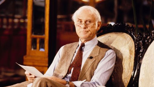 Loriot sitzt in einem Sessel und hält ein Blatt Papier. 